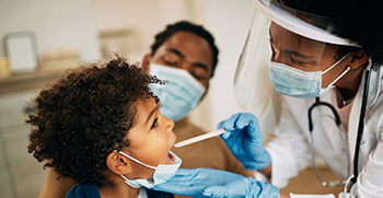 A child getting swabbed by a doctor, with his mother sitting with him